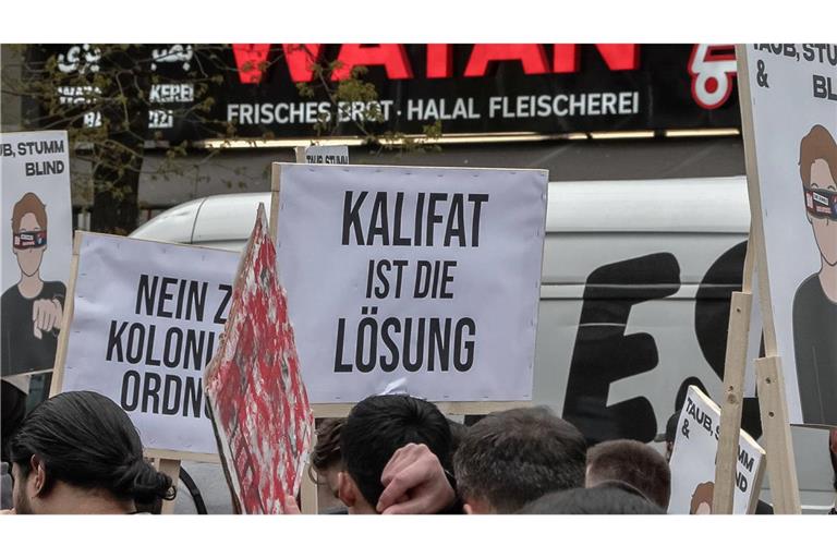 Teilnehmer einer Islamisten-Demo halten ein Plakat mit der Aufschrift „Kalifat ist die Lösung“ in die Höhe.